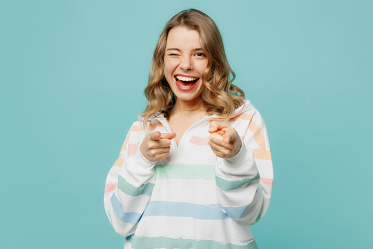 Young cheerful happy blonde woman wear hoody point index finger camera on you motivating encourage wink blink eye isolated on plain pastel light blue cyan background studio portrait Lifestyle concept