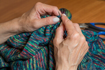 hands of woman knitting handmade clothes with spokes using  wool yarn. Concept of leisure activity.Knitting from yarn on  coarse spokes.