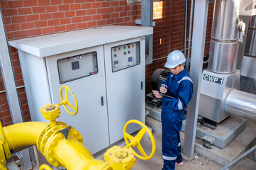 Young engineer working at large factory,Technician in protective uniform and with hardhat  checking temperature in pipes