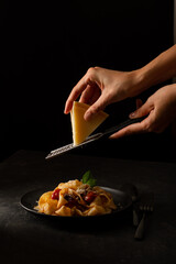 Italian pasta fettuccine with parmesan on a black plate. Person grates cheese.