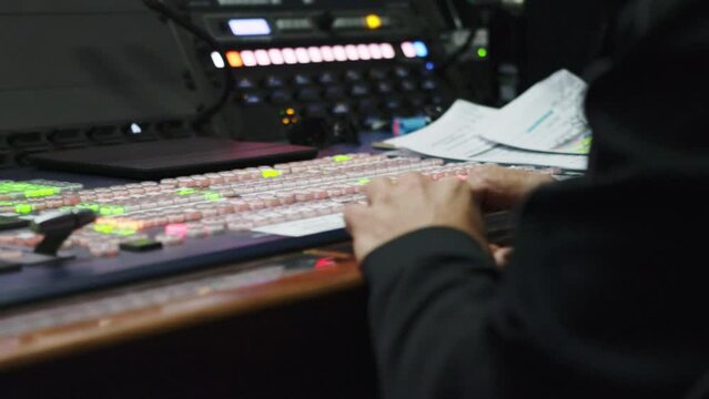 Workstation with vision mixer for managing videos in broadcasting control room. Man hands against control console closeup