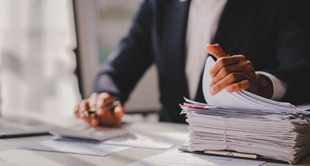 work from office A businessman works a bunch of paper files to find information on his desk at...
