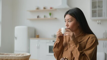 Relaxed girl Asian korean woman in domestic kitchen with cup of coffee drinking hot herbal tea multiethnic lady thoughtful calm housewife drink beverage looking in distance dreaming with mug in hands