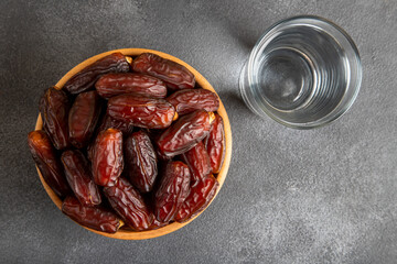 Glass of water with a bowl of date fruit on black background
