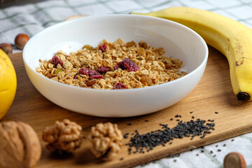 Granola with cranberries and almonds in a white bowl . Fresh banana and apple, walnut, seeds  on wooden table.   Health food concept. Breakfast food background
