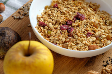 Granola with cranberries and almonds in a white bowl . Fresh banana and apple, walnut, seeds  on wooden table.   Health food concept. Breakfast food background
