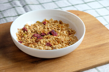 Granola with cranberries and almonds in a white bowl on a wooden cutting board.  Health food concept.
 Breakfast food background