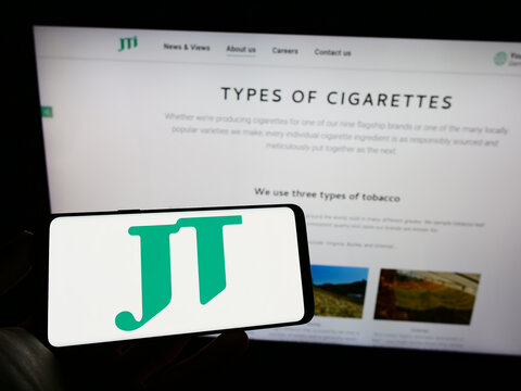 Stuttgart, Germany - 03-07-2023: Person holding cellphone with logo of cigarette company Japan Tobacco Inc. (JT) on screen in front of business web page. Focus on phone display.