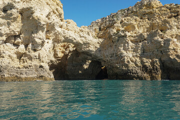 Stone Cliff caves in Portugal on a sunny day from the boat with teal water
