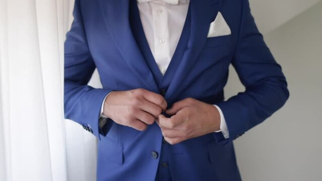 Closeup shot of a bridegroom holding his blue costume while standing near a window