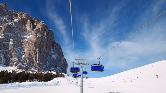 First-person view FPV point of view POV of cable chair ski lift ascend for alpine skiing in Dolomites. Ski resort piste with people skiing in Dolomites in Italy. Ski area Belvedere. Canazei, Italy