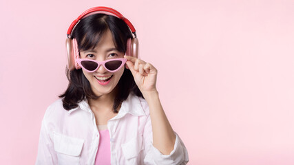 happy young asian woman model with stylish trendy sun glasses enjoy listening music by headphone audio and dancing isolated on pink studio background. technology, girl fashion, accessory concept.