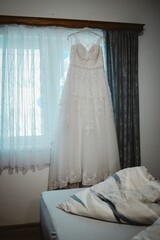 Bridal gown hanged alongside window curtains