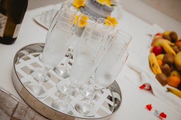 Fototapeta na wymiar High-angle of empty champagne glasses on the tray with a cake and fruits in the blurred background