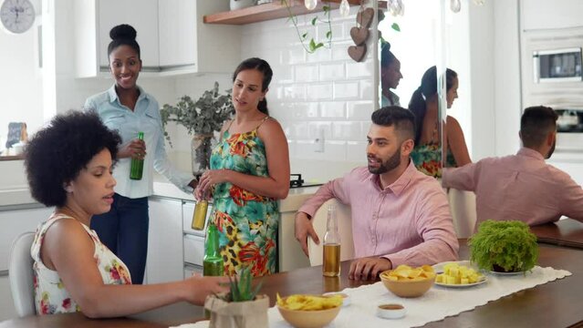 Small party, friends in kitchen talking and laughing. Young adults drinking bier and having fun at home.