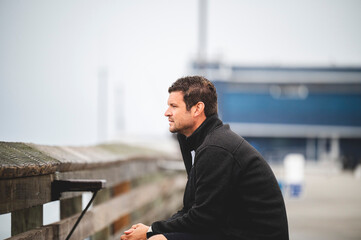 Fototapeta premium Caucasian man sitting on a bench on the pier against blurred background