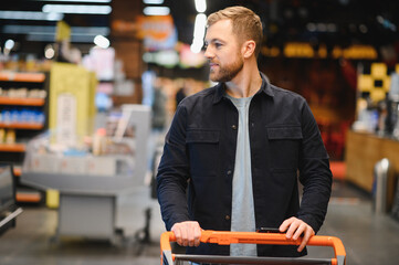 Portrait of smiling man walking with his trolley on aisle at supermarket.