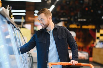 Young man buying groceries at the supermarket. Other customers in background. Consumerism concept.