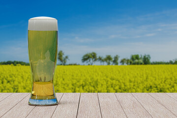 Glass of light beer on the table against view of field with yellow flowers and blue sky.