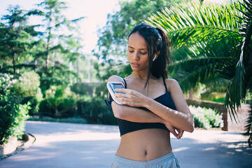 Ethnic woman using smartphone in armband in park