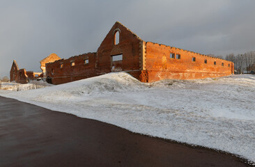 The ruins of an old brick building illuminated by the evening sun. Architectural monument. Road. Hillock. Snow cover
