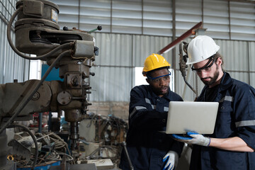 Two male technician using laptop computer for checking lathe machine in factory, maintenance CNC machine in workshop