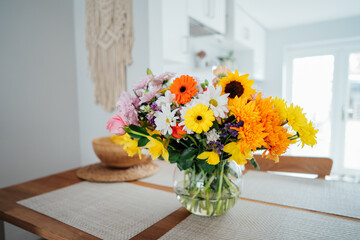 Kitchen counter table with focus on vase with huge multicolor various flower bouquet with blurred background of modern cozy white kitchen. Home interior design details. Mother's day. Copy space.