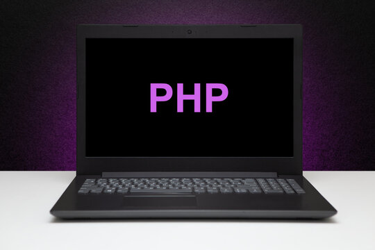 PHP text on laptop screen on textured black background with purple light. Learn php programming language, computer courses, training.