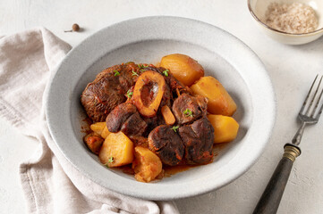Stew veal shank meat Ossobuco. Traditional Italian Ossobuco alla Milanese served with stew potatoes and vegetables on a white stone background. Horizontal crop