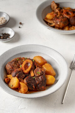 Stew veal shank meat Ossobuco. Traditional Italian Ossobuco alla Milanese served with stew potatoes and vegetables on a white stone background. Vertical crop