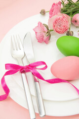 Happy Easter celebration table. Easter eggs and flower decoration on plates, pink background.