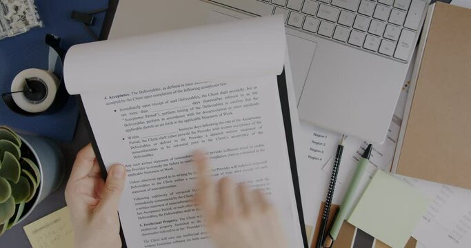Top view of hands holding business contract on clipboard with laptop and desk in background. Paperwork and businessperson concept.