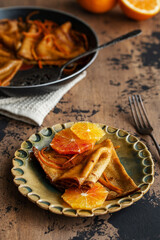 Traditional French Crêpes suzette pancakes with orange sauce in a pan with oranges on a rustic wooden background. Selective focus. Maslenitsa festival meal.