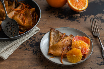 Traditional French Crêpes suzette pancakes with orange sauce in a pan with oranges on a rustic...