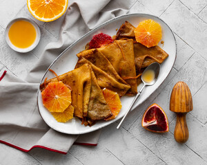 Traditional French Crêpes suzette pancakes with orange sauce on a serving dish on a light grey...