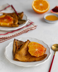 Traditional French Crêpes suzette pancakes with orange sauce on a serving dish on a light grey...
