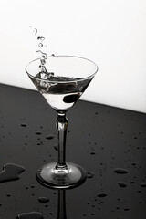 Green olive falling into martini glass with splashes on a black-white background. 