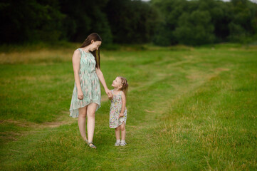 Naklejka na ściany i meble Portraits of joyful mother and daughter spend time together, enjoy happy family time, walk in the park. The concept of a happy family, family day,mother's day, countryside vacation, unity with nature.