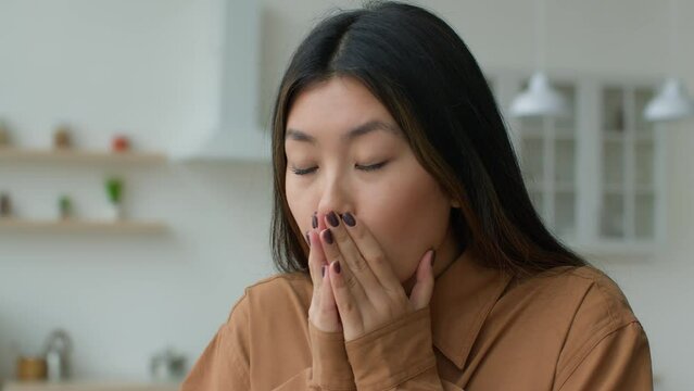 Unhealthy sick Asian woman girl sneeze cover face with hands in kitchen Japanese businesswoman suffer runny nose has allergy covid-19 symptom fever flu Korean lady feeling bad sneezing cold at home