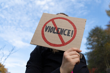 Woman holding a cardboard banner sign with word Violence strikethrough. Female protester with Stop...