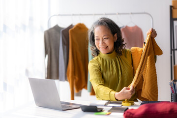 Asian senior female online seller reviewing shirt video live streaming to social media at home.