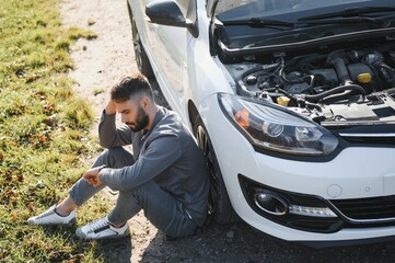 Sad driver holding his head having engine problem standing near broken car on the road. Car breakdown concept