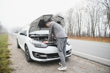 young stressed man having trouble with his broken car looking in frustration at failed engine
