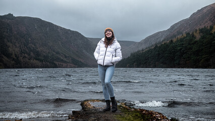 Woman standing on a piece of land in front of a lake during stormy weather in the mountains