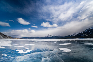 frozen abraham lake with cracked ice and sky reflected in ice with mountains on background