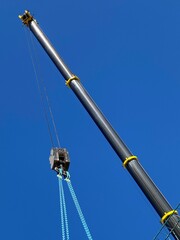 Telescopic crane at a construction site under a blue sky, a vertical shot
