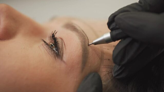 A woman master makes permanent eyebrow makeup to a young beautiful girl in a beauty salon.Microblading, eyebrow tattoo in a beauty salon.