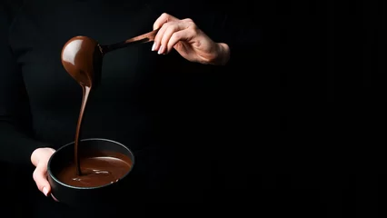 Zelfklevend Fotobehang The chef scoops hot chocolate into a bowl. On a black background. Preparation of chocolate. © Yaruniv-Studio