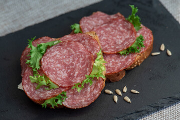 sliced ​​salami and lettuce on black background, top view. open sandwiches with sliced ​​salami sausage on rye bread