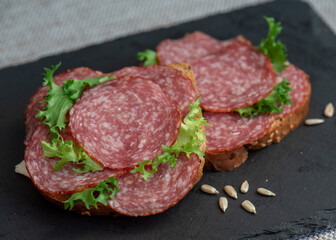 sliced ​​salami and lettuce on black background, top view. open sandwiches with sliced ​​salami sausage on rye bread
